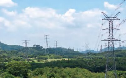 Hochspannungsmasten und Freileitungen über bewaldetem Hügelland aus der Luft