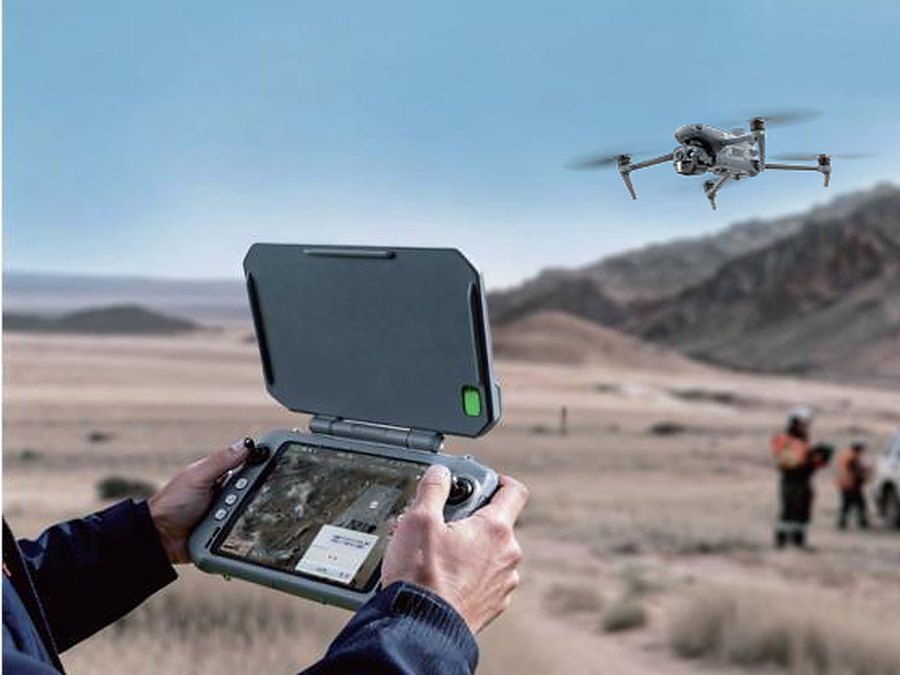Einsatzkraft steuert eine Autel EVO III über das Controller-Display, die Drohne fliegt im Hintergrund über dem Einsatzgebiet